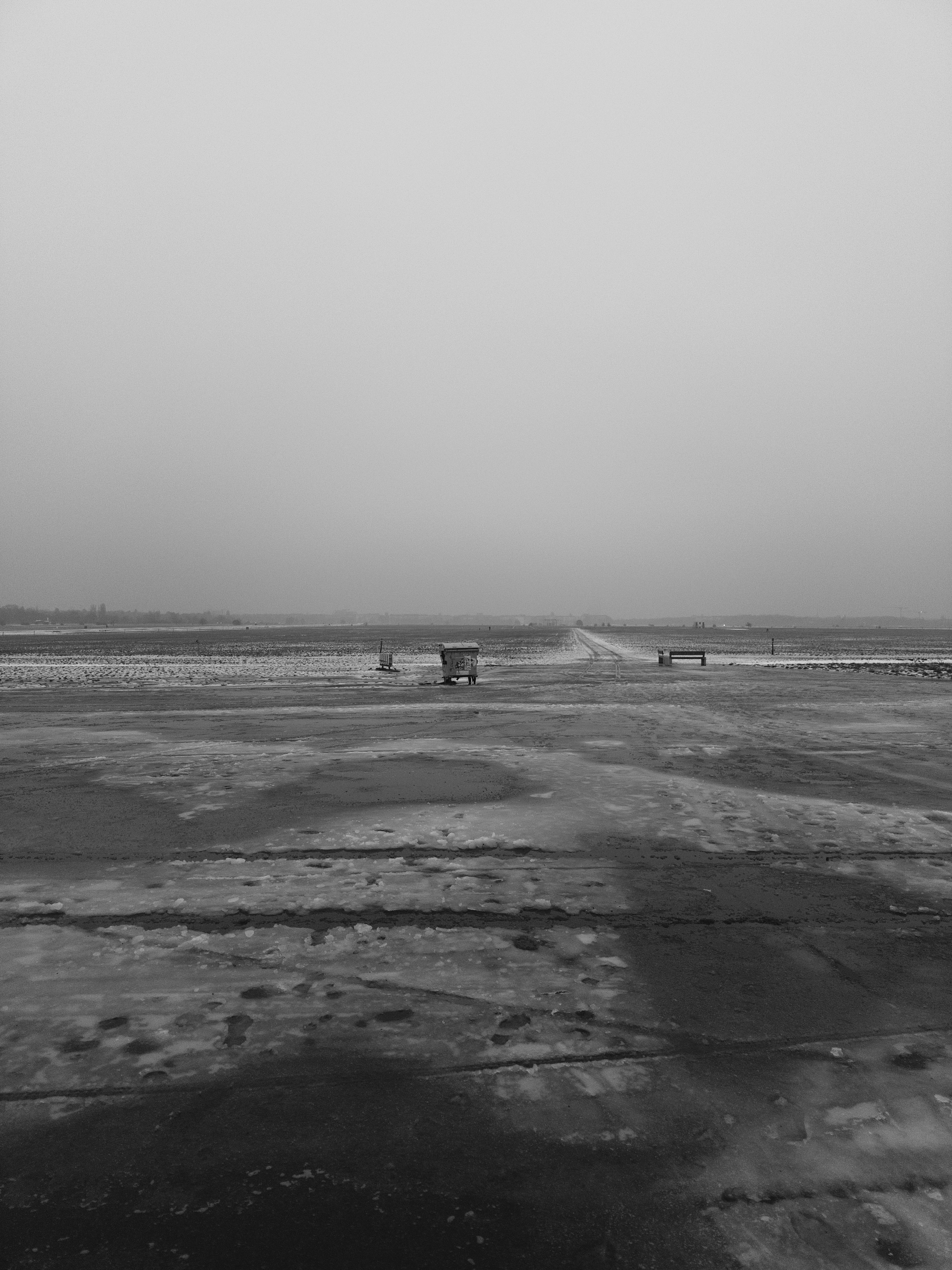 Ein Schwarz-Weiss-Foto: Das Tempelhofer Feld ist von Eis und Schneematsch bedeckt, es wirkt trist. In der Mitte eine Mülltonne.